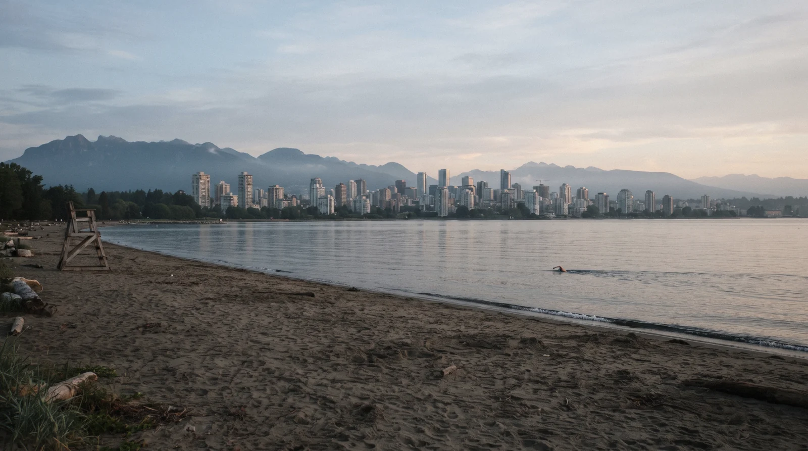 Swimmers in the long saltwater pool beside the sand at Kitsilano Beach Vancouver with the downtown towers across the water