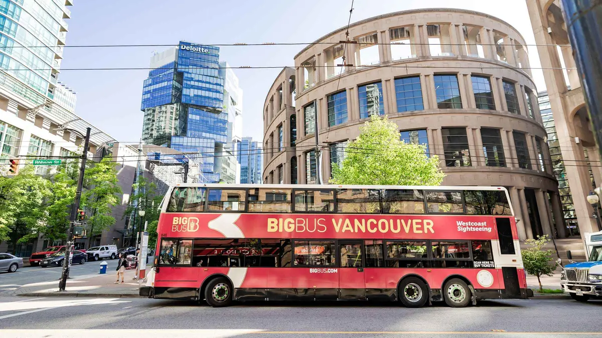 Red double-decker sightseeing bus passing Canada Place, Vancouver hop-on hop-off tour by double-decker bus
